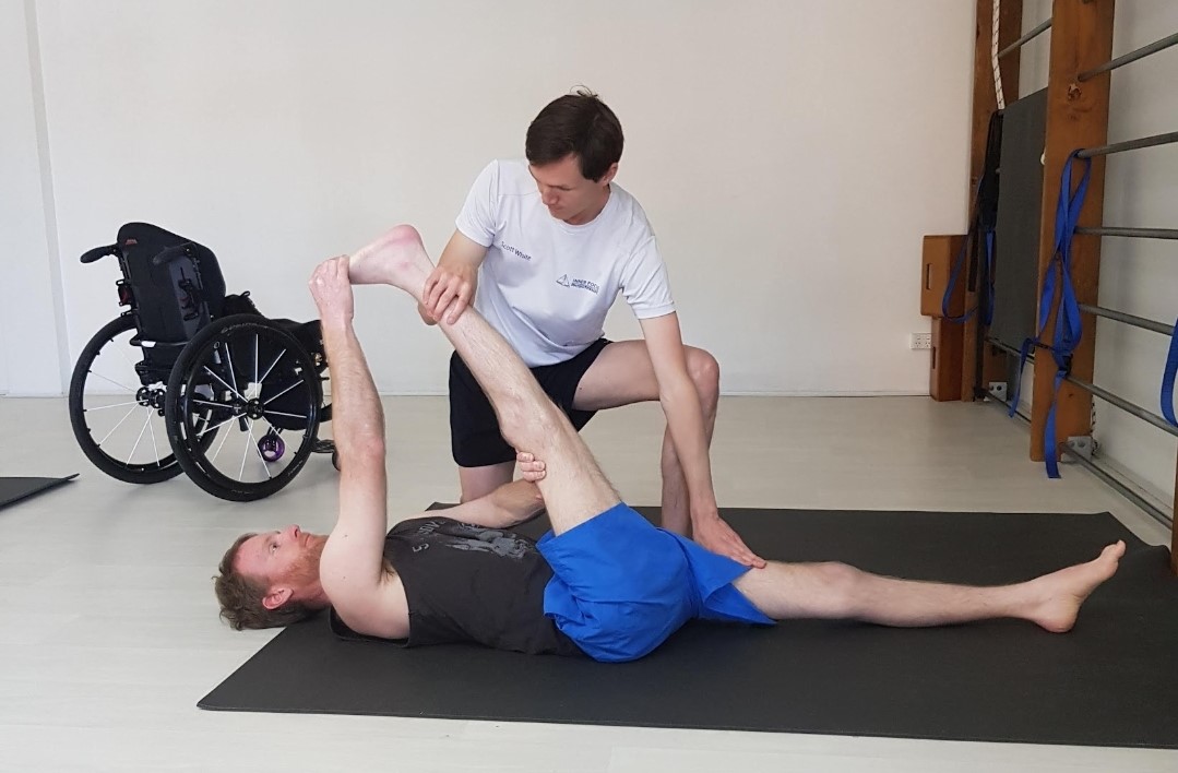 A practitioner stretches out a man's leg on an exercise mat